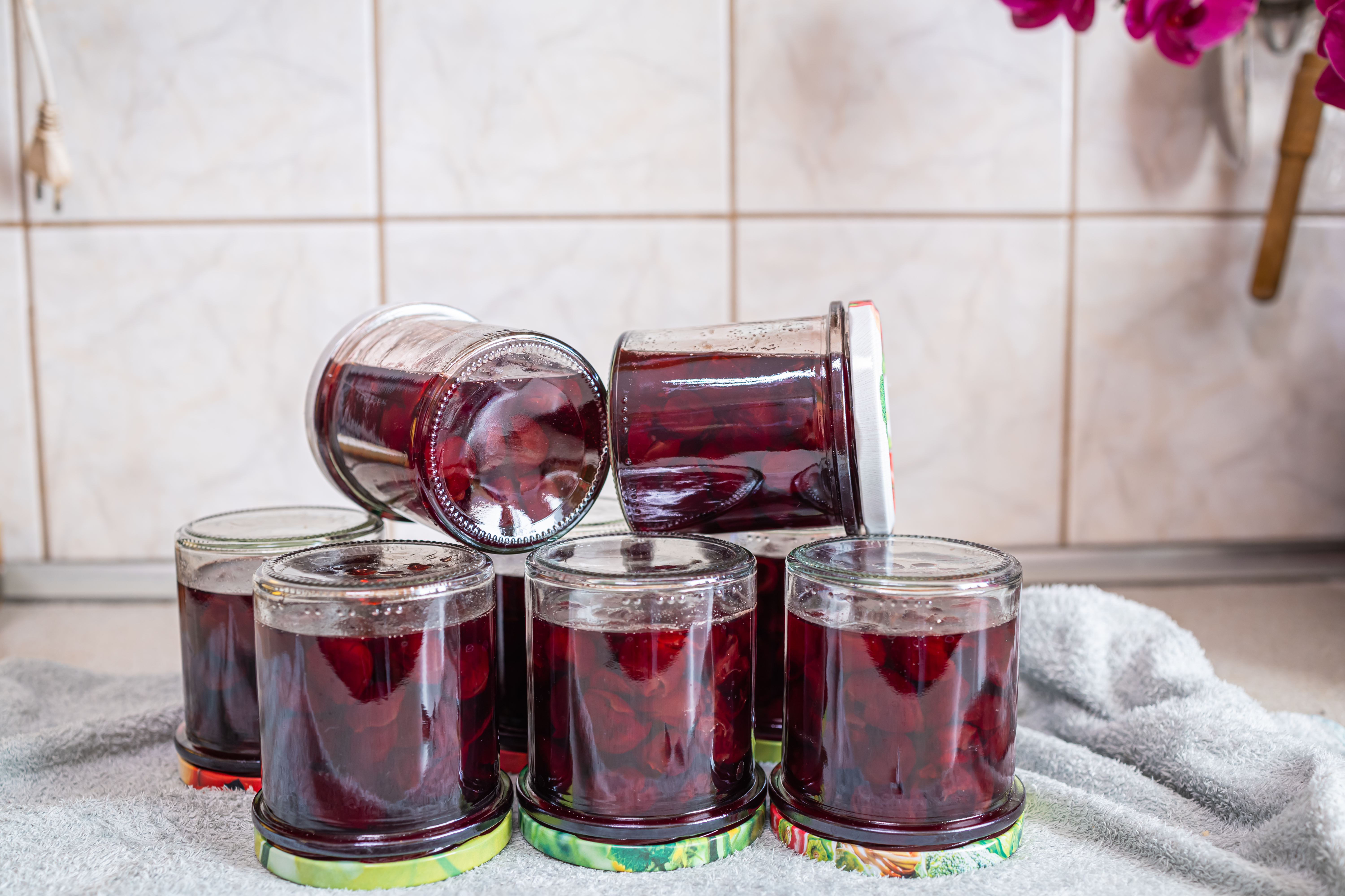 Beautiful arrangement of homemade cherry preserves in sealed glass jars on a kitchen surface. Rich ruby-red fruit jam made from ripe cherries using traditional home preserving methods.